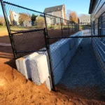 a fenced in area with dirt and building in the background